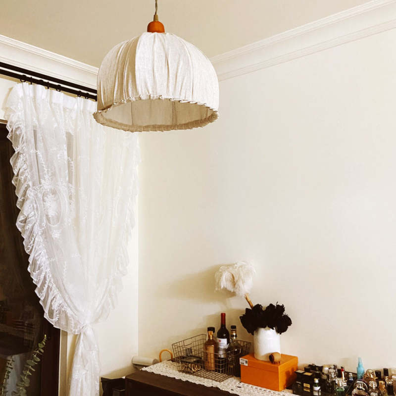 Beige fabric pendant above a dresser beside a lace curtain