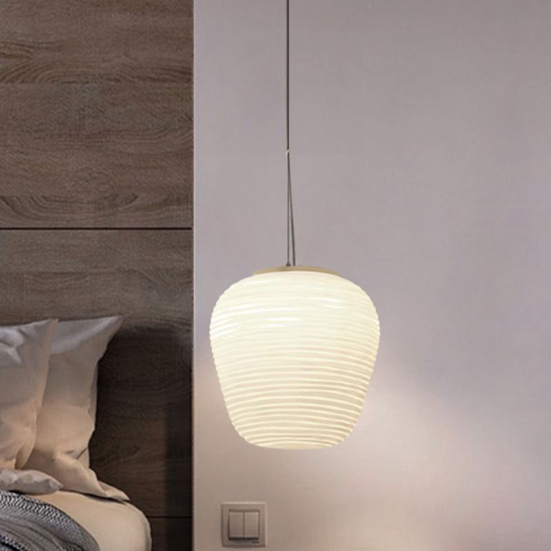 Short rounded ribbed white pendant glowing beside a bed, wood headboard and wall switch