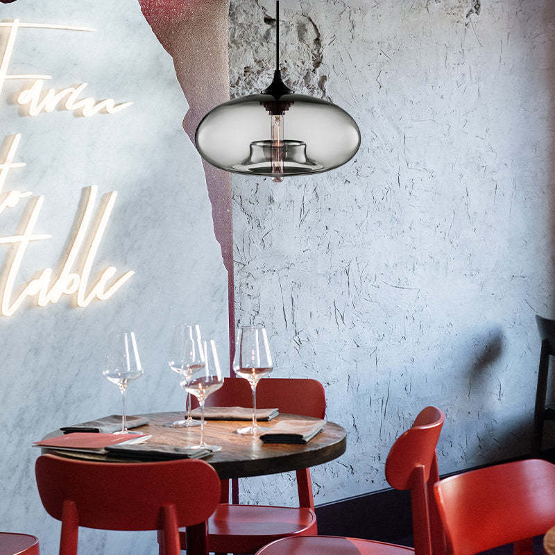 Gray-toned glass pendant above a round table with Red chairs, wine glasses and menus against a textured Blue wall