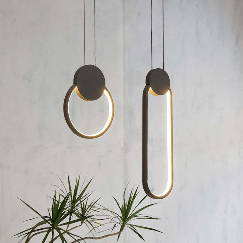 Dark circular and long oval loop pendants with illuminated inner edges above a leafy plant