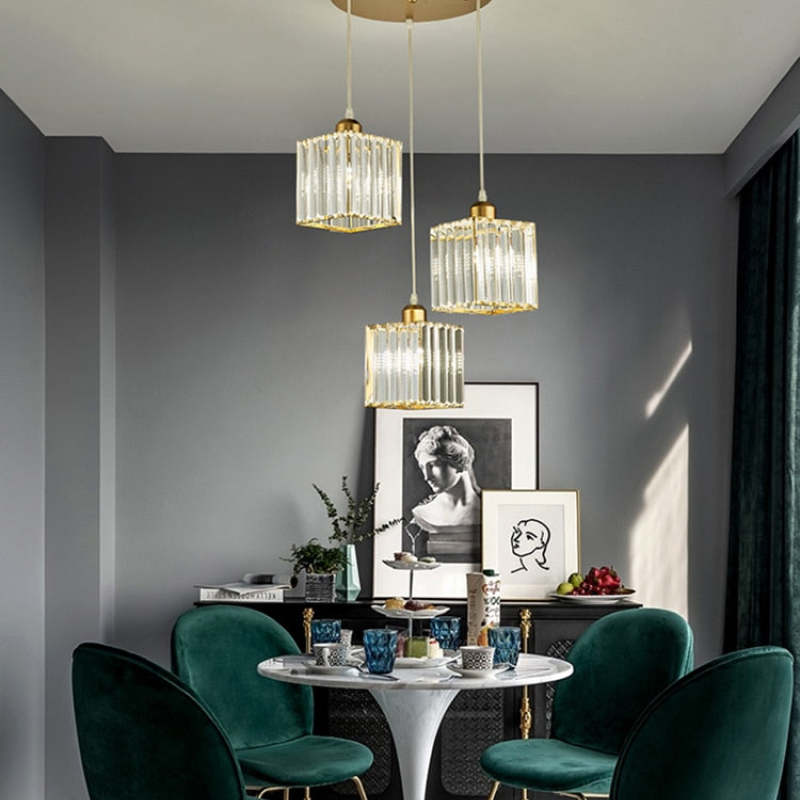 Three gold Herbert square glass shades below a round canopy above a table with green chairs and portrait artwork