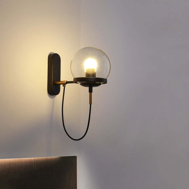 Black Alessio glass globe wall light above a bed headboard