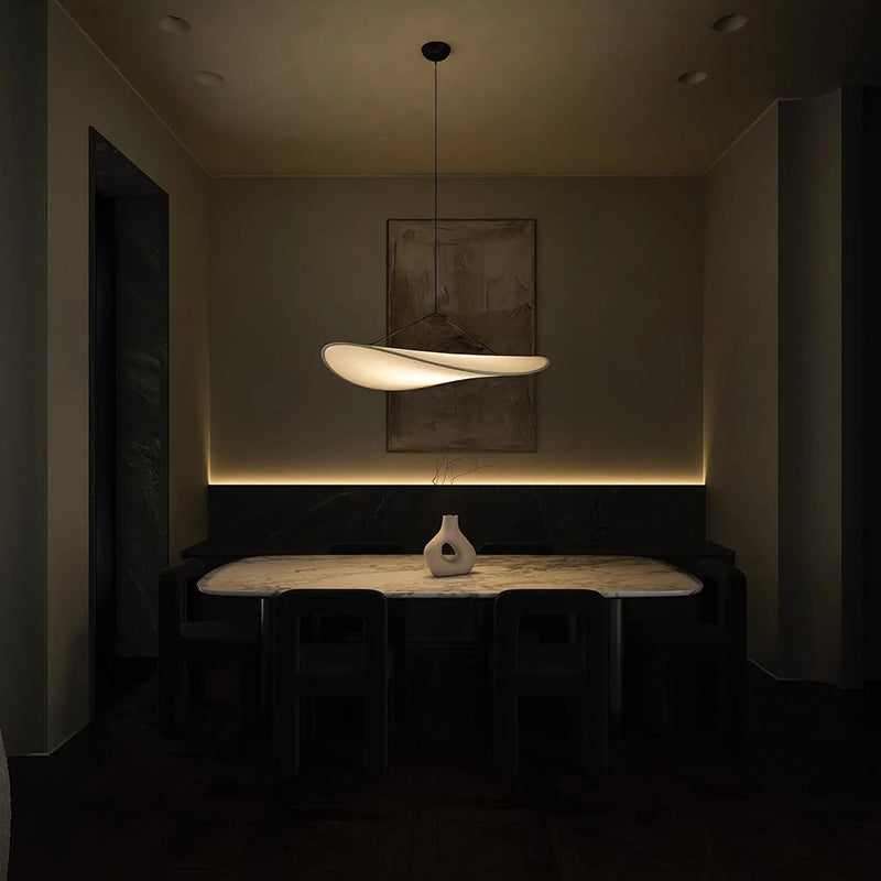 Illuminated Renée pendant above a dining table with dark chairs and separate wall accent lighting