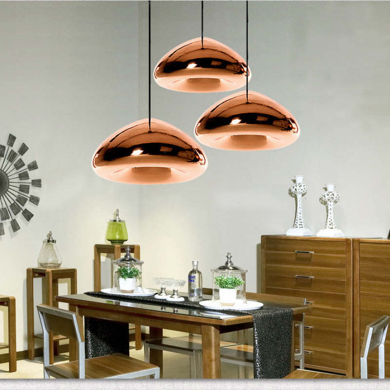 Three rose-gold glass pendants above a wooden dining table