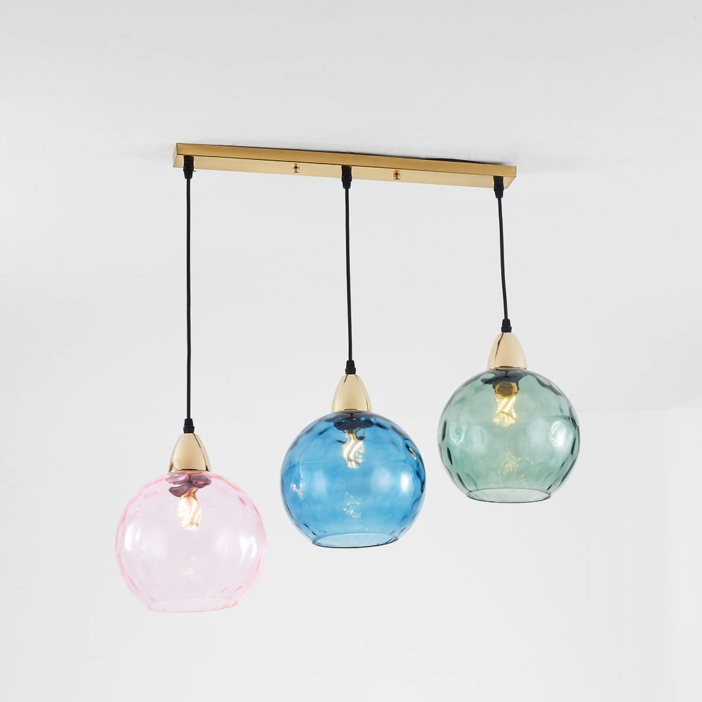 Pink, blue and green rippled glass globes on black cords below a gold-tone straight bar