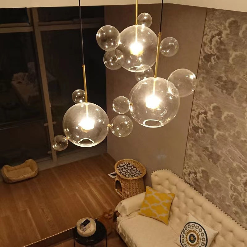 High-angle living-room view of several clear bubble pendants above cream tufted sofa, yellow cushions and wood floor