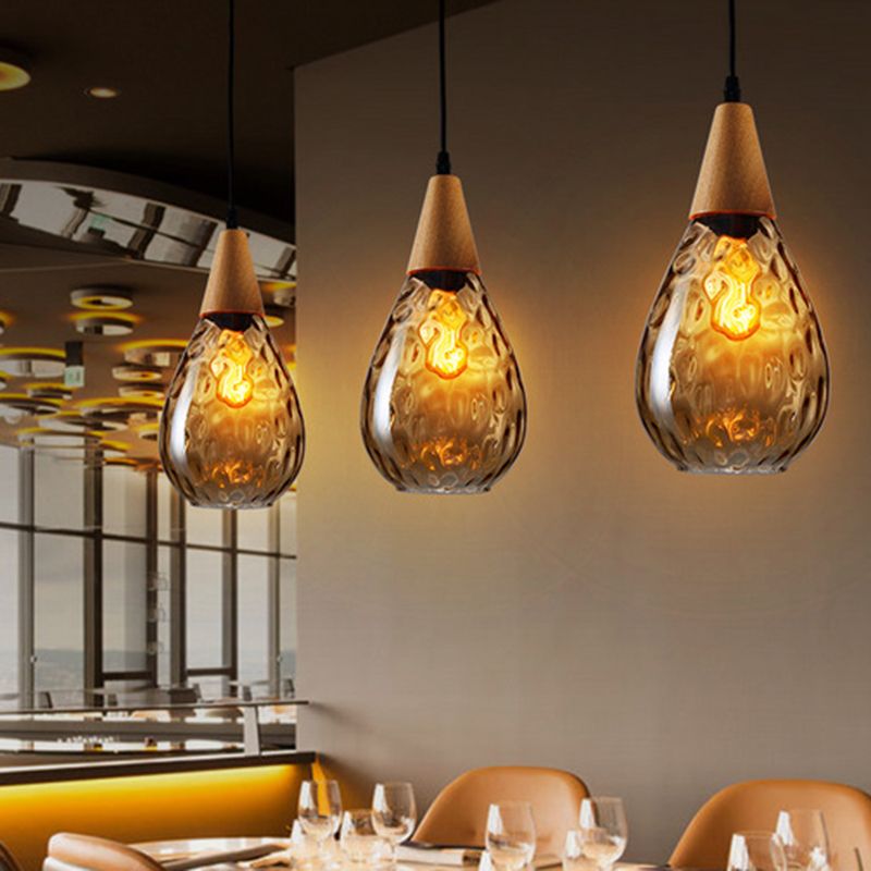 Three amber Avi pendants with wood tops above restaurant table with glasses and tan chairs