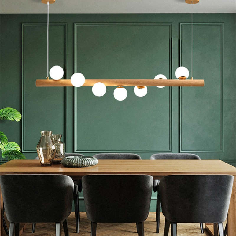 Light wood seven-globe pendant above a wooden table with Gray chairs, metallic vases and a Green paneled wall