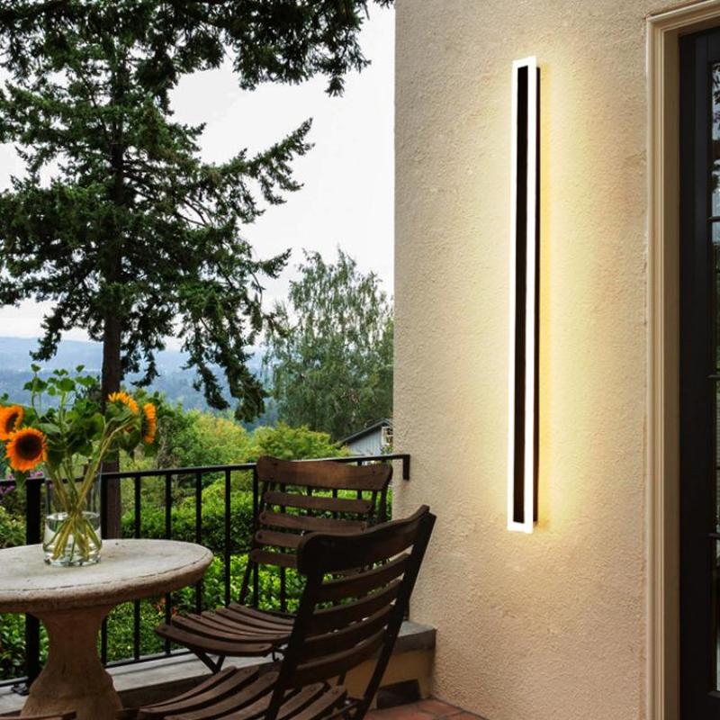 Long Edge wall light on a pale exterior wall beside a wooden chair and round patio table