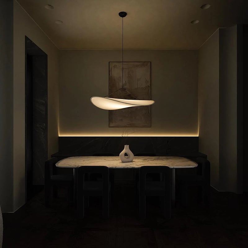 Illuminated leaf-like pendant above a dining table with black chairs and a white sculptural vase