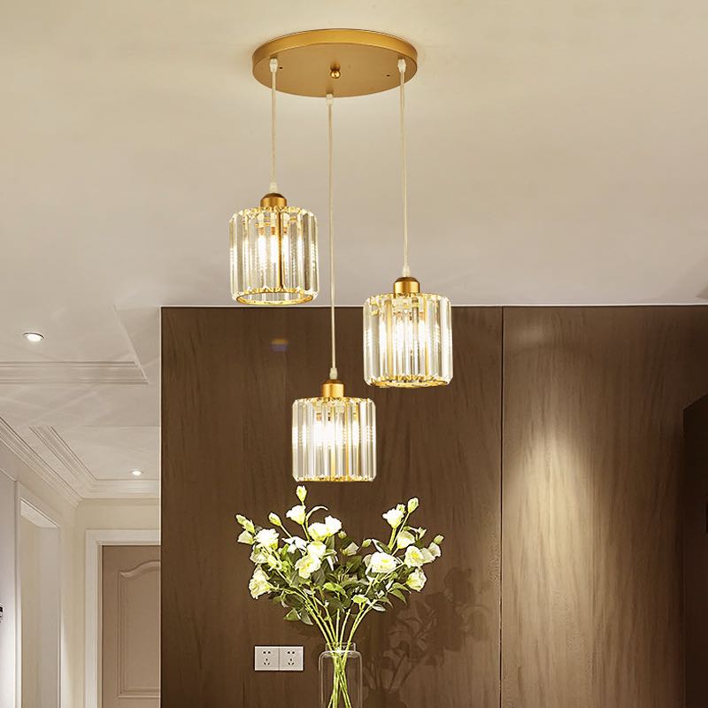 Three gold Herbert cylindrical glass shades staggered below a round canopy above flowers and a sideboard