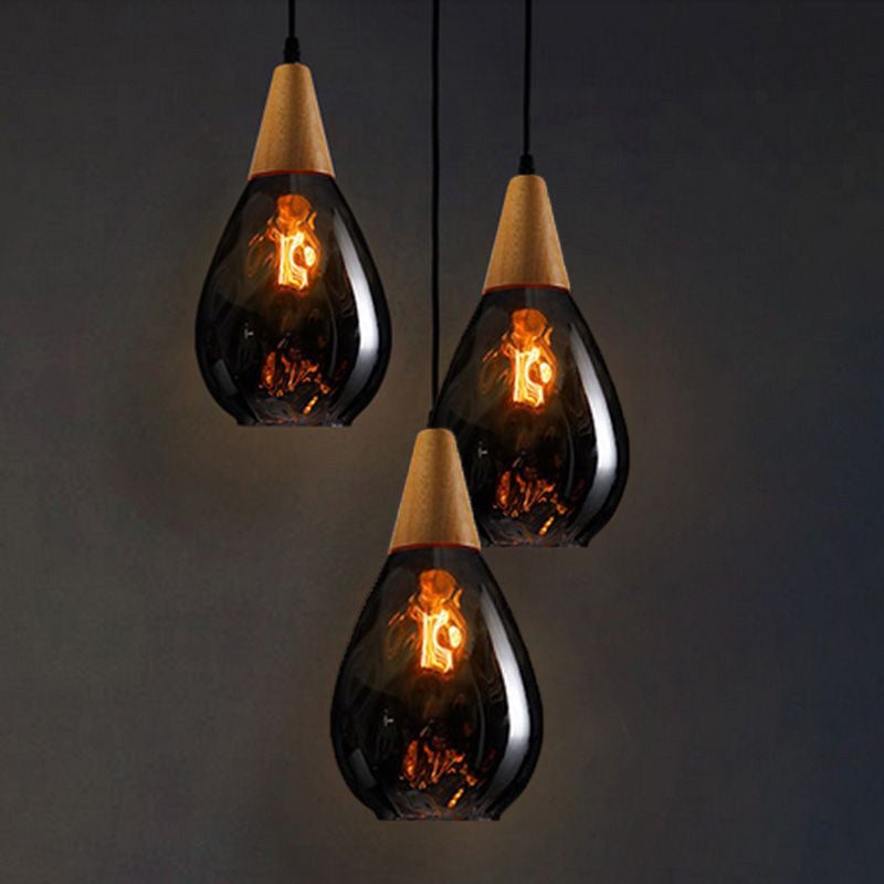 Three slender smoke-grey Avi pendants with wooden caps and glowing lamps at staggered heights on dark background