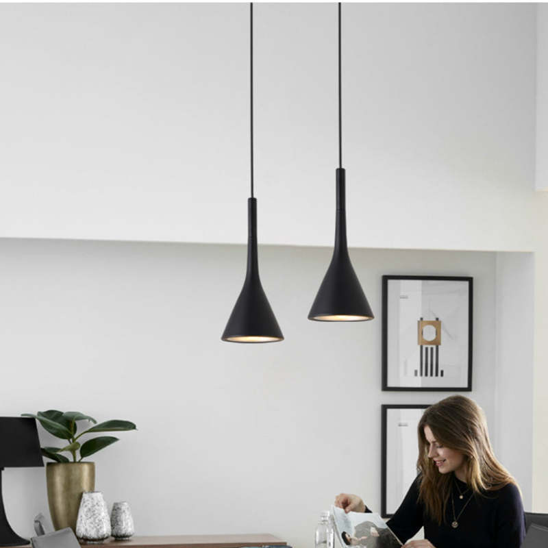 Two black cone pendants at different heights above a table beside a woman reading and potted plants