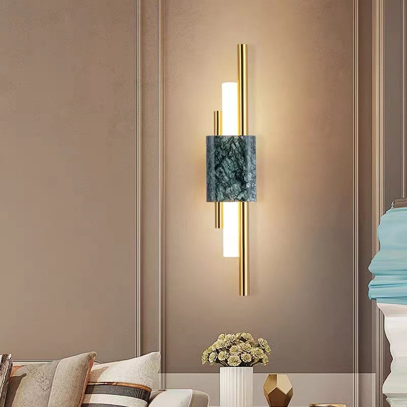 Green-veined Alana wall light with gold-tone rods and a lit bar above flowers beside a sofa on a pale wall