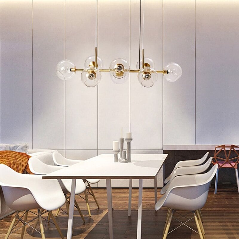 Frontal gold clear-globe pendant above white dining table, white chairs and candlesticks against pale panelled wall