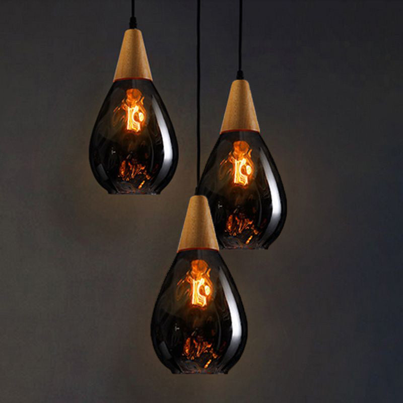 Three narrow smoke-gray Avi pendants with wood tops and visible lit bulbs at staggered heights against dark wall