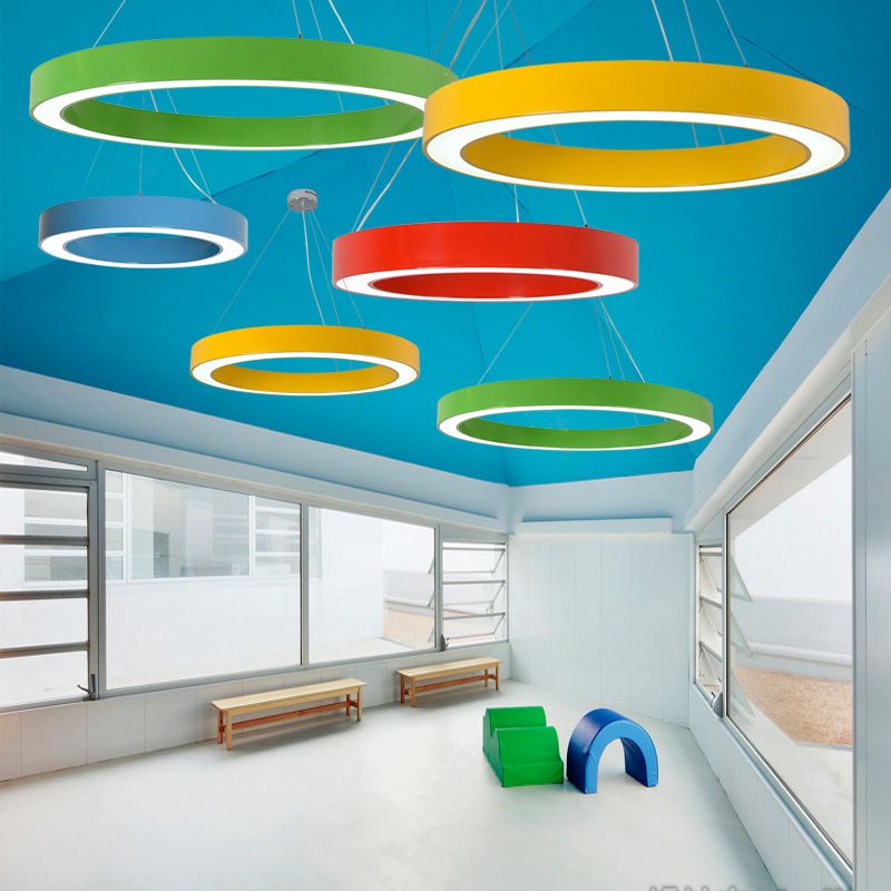 Six separate coloured rings below blue ceiling in room with benches, large windows and soft play forms