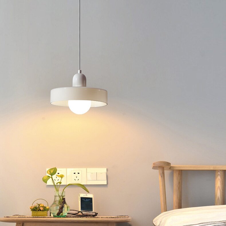 Cream-and-white ring pendant lighting a bedside ledge with plants and a phone beside a wooden headboard