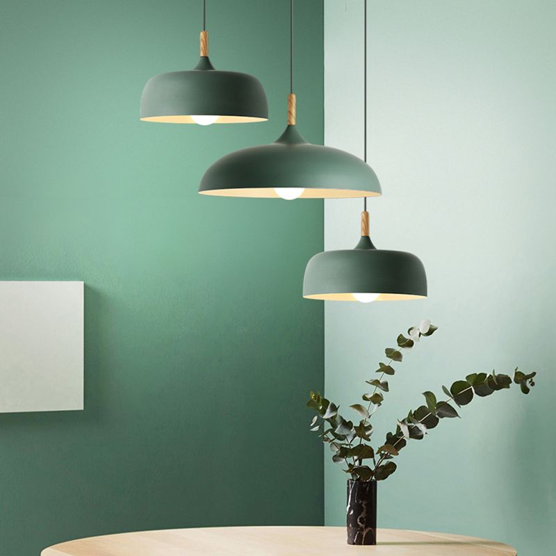 Three green dome pendants in two profiles above a round wooden table with a leafy branch arrangement