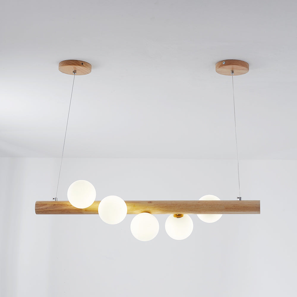 Light wooden bar pendant with five White globes, Gold-toned collars, two cables and round canopies against a light interior