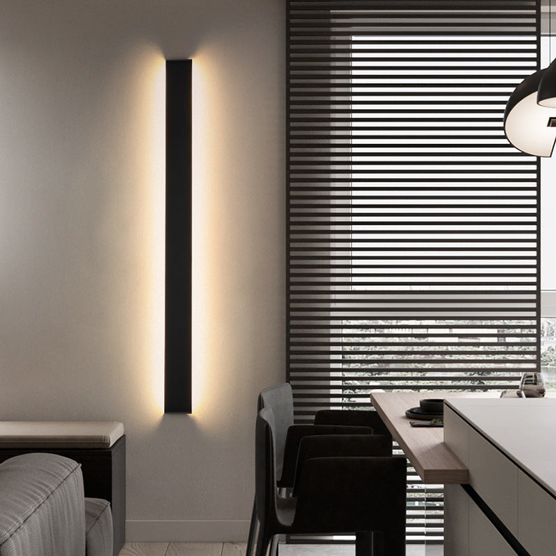 Vertical black wall light beside a bed and window blinds