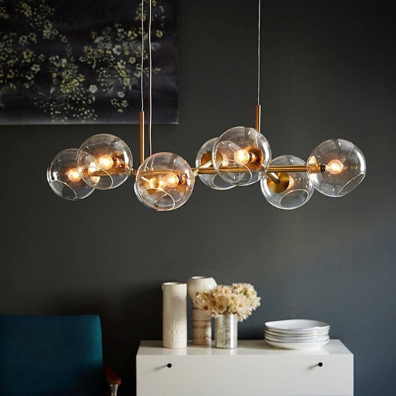 Gold body and clear globe pendant above white sideboard with vases, flowers and plates against dark wall with artwork