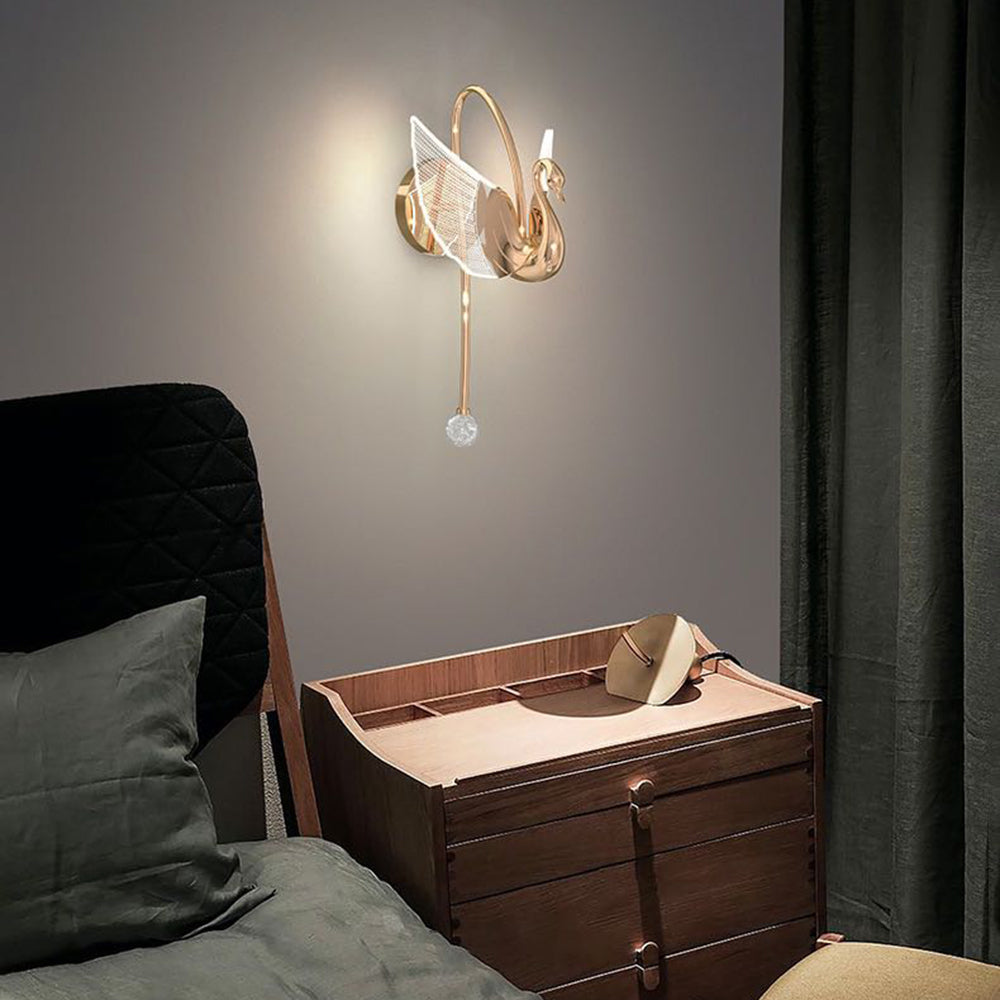 Rose-gold-looking swan wall light above wooden bedside drawers beside a dark upholstered bed and curtains