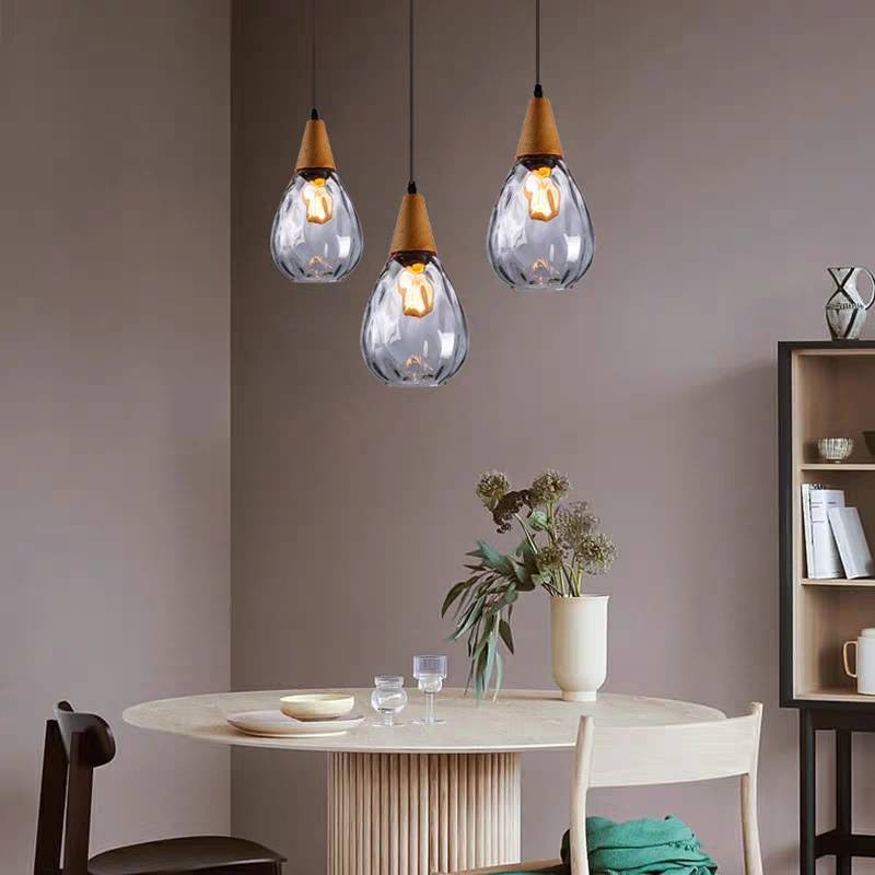 Three clear Avi pendants at staggered heights above round dining table, chairs, flower vase and shelves