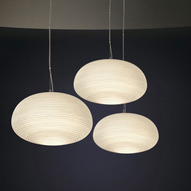 Three wide flattened oval ribbed white pendants glowing at different hanging heights