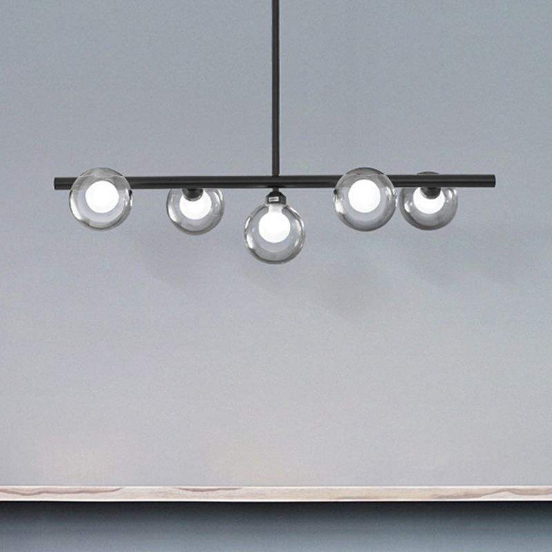 Black five-globe pendant with a lower central globe illuminated against a textured pale wall