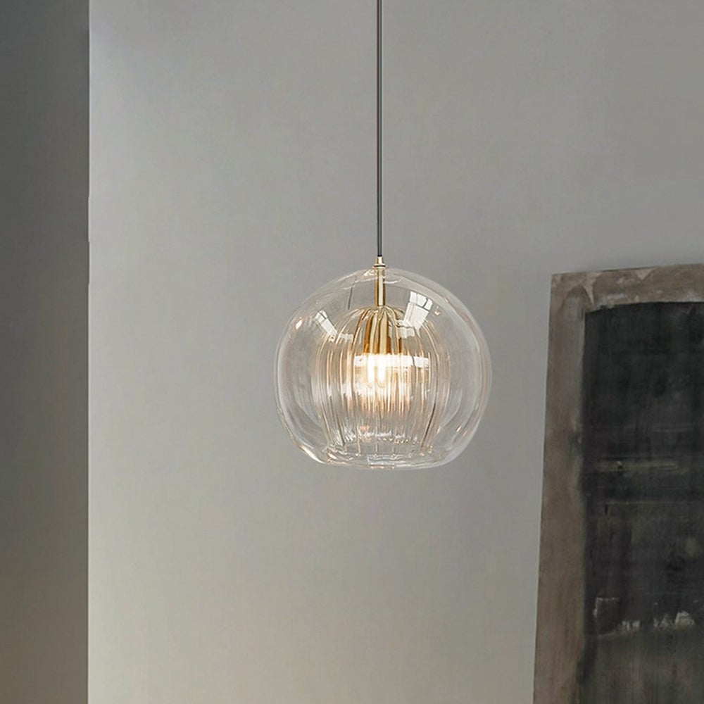 Single clear globe pendant beside a pale wall and dark stone panel