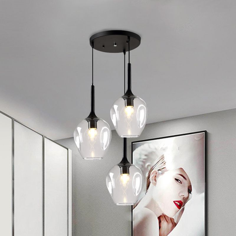 Clear glass cluster pendant with three rounded shades beside a large portrait on a light wall