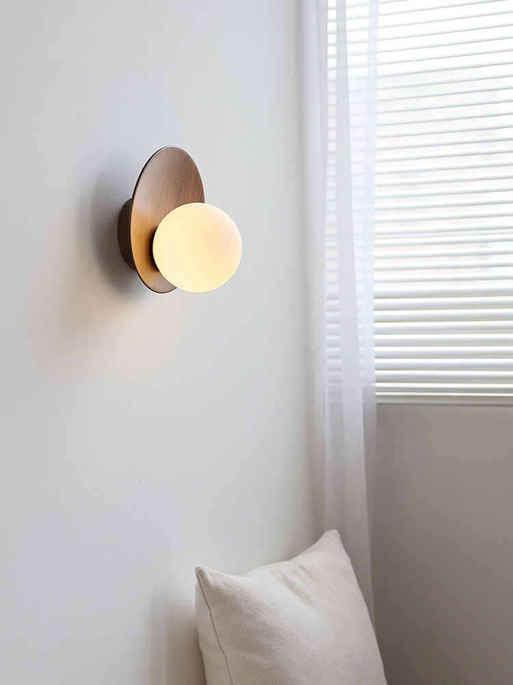 Illuminated Lunetta walnut-disc wall lamp beside window blinds
