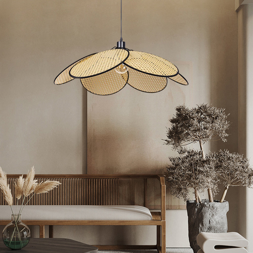 Black-trim woven petal pendant above a wooden bench with cream seat, beside a potted tree and dried-grass vase