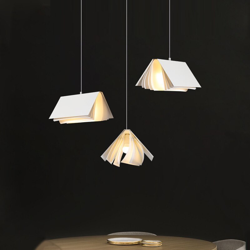 Three separate White Sienna book-style pendants above a round wooden dining table against a dark wall