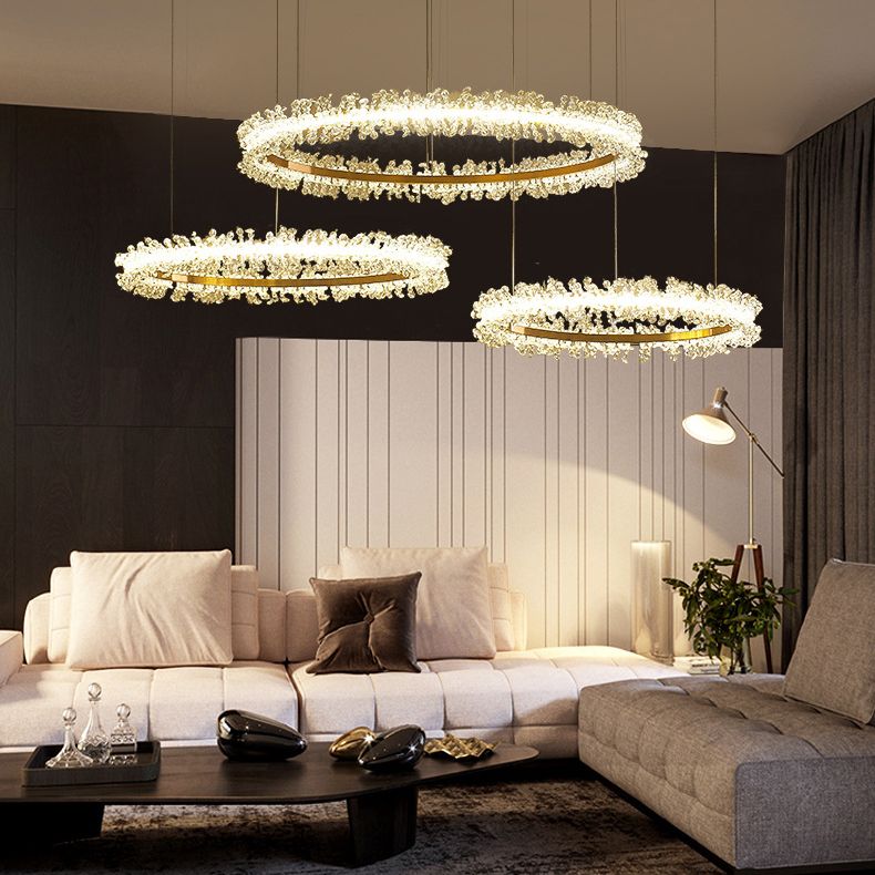 Kristy three-ring pendant light above a pale sectional sofa beside dark wall panels and a white curtain.