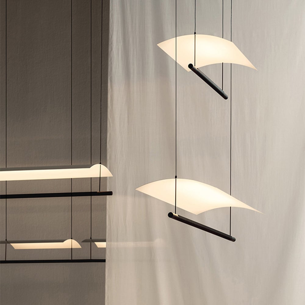 Angled end views of short and long Edge pendants with glowing cream curved shades and black lower bars beside curtains
