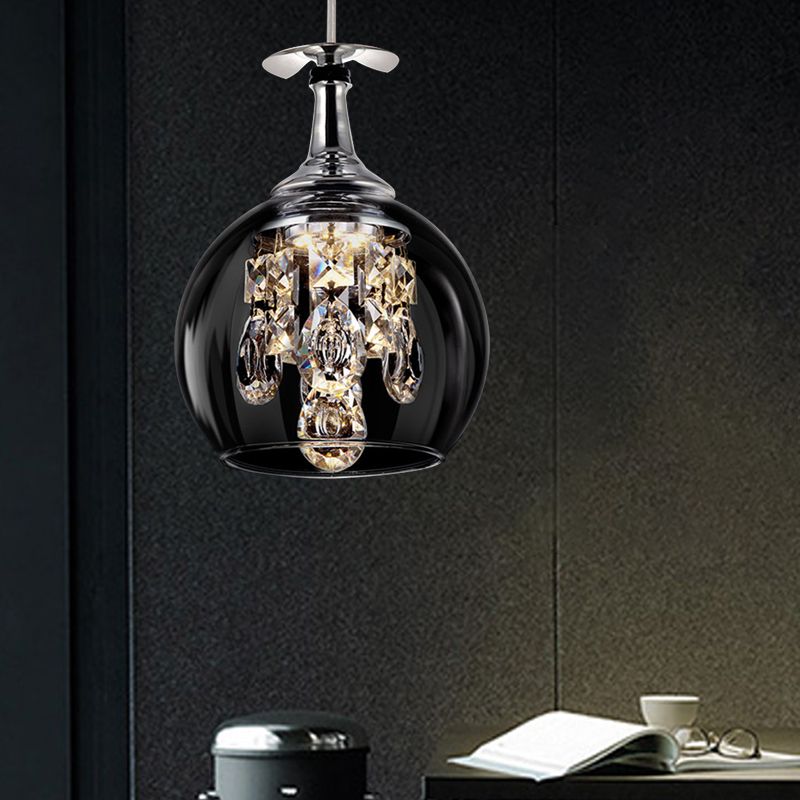 Single rounded Kristy glass pendant with crystal drops above a book, cup and glasses on a dark tabletop.