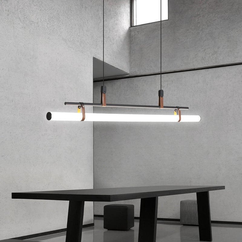 Black linear pendant above a long black table and cube stool in a concrete room with a mirror and high window