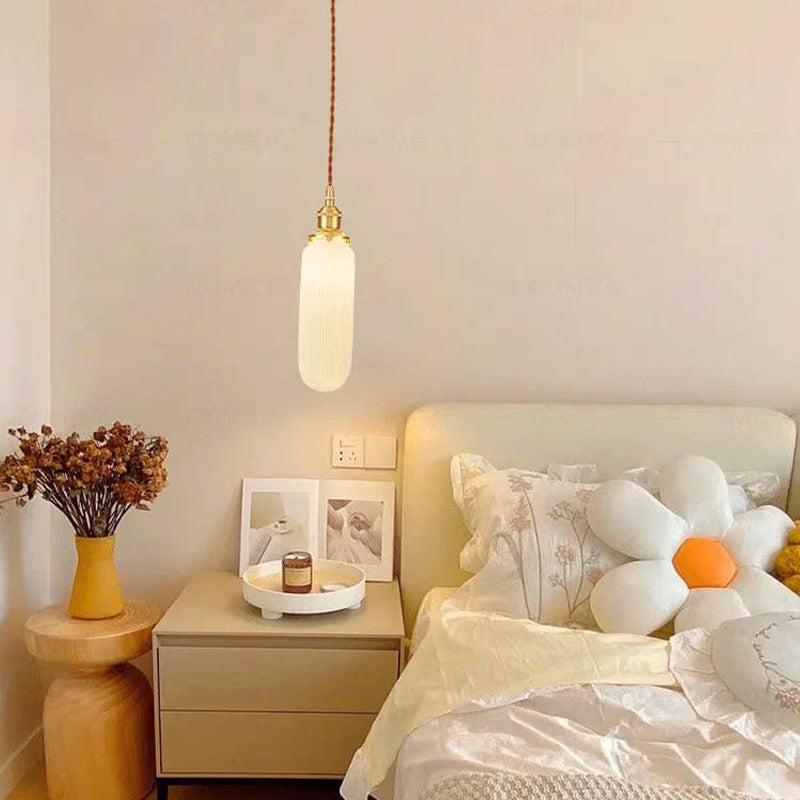 Slim white cylindrical Valentina pendant beside a bed and flowers