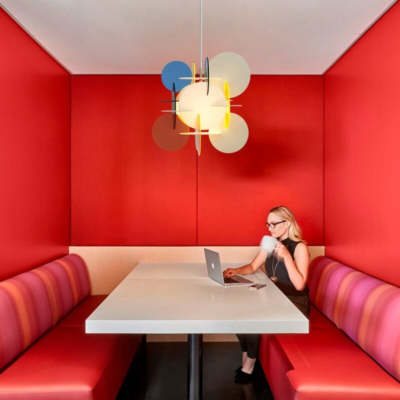 Morandi Yellow/Blue/Red pendant above a white table in a red booth, with a person using a laptop