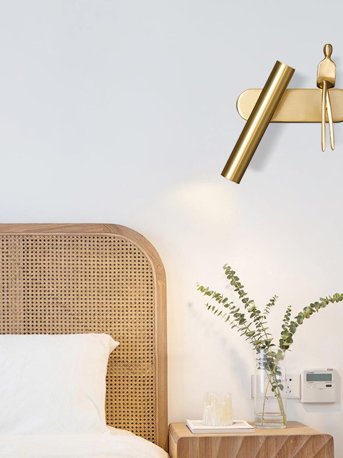 Brass-coloured figure wall light above a rattan headboard and wooden nightstand with a vase
