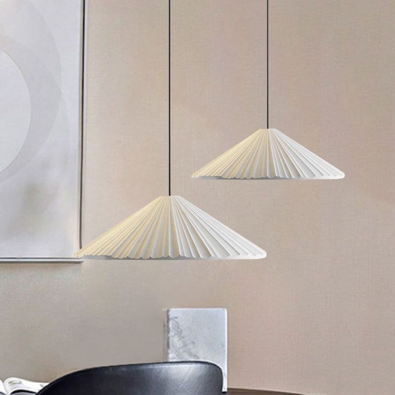 Two white shallow pleated pendants at different heights near framed art above a table and black chair