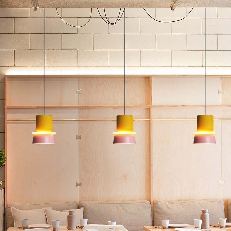 Three separate Morandi Yellow Pink tall-cup pendants above a booth dining area, with black cords and loose overhead cable loops