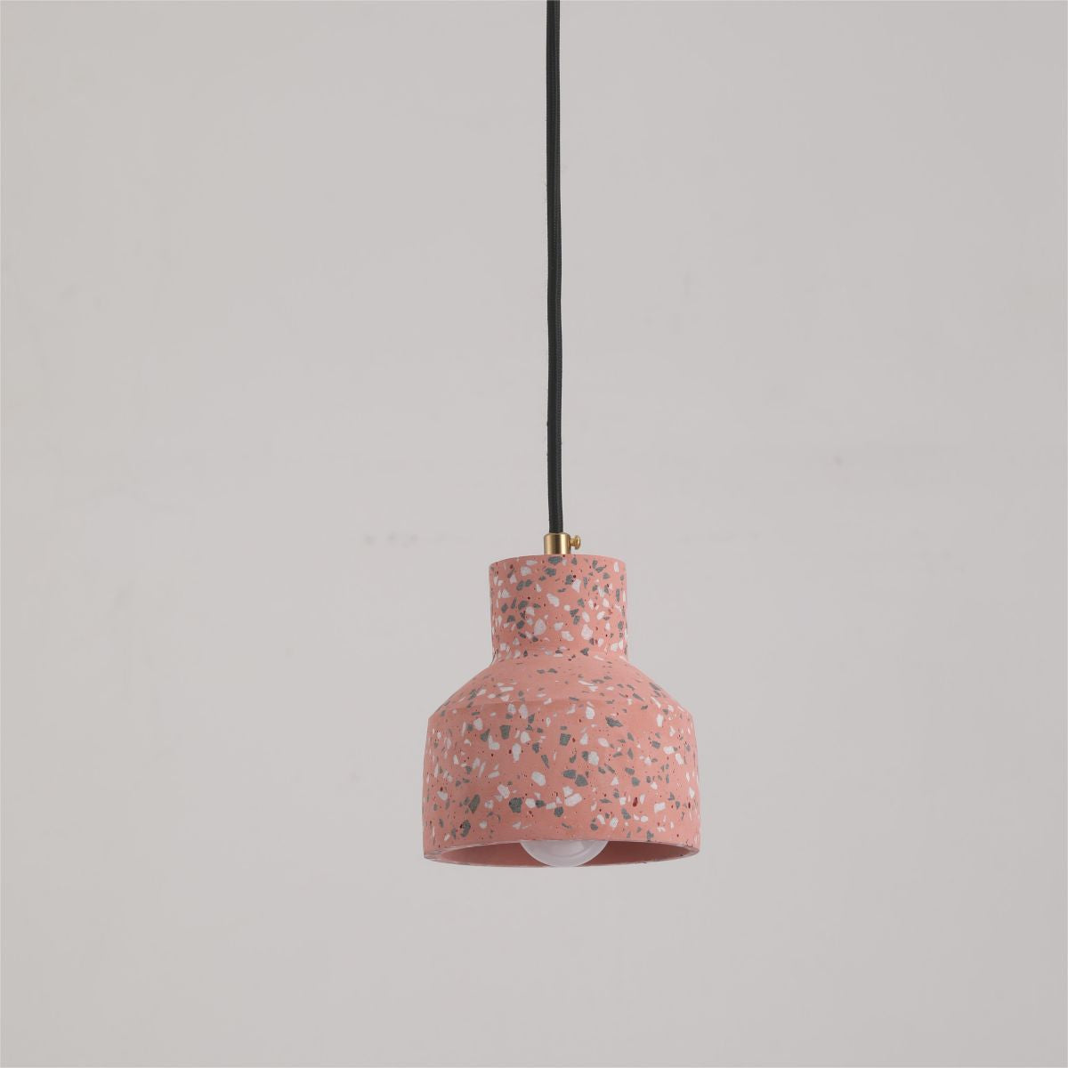 Red-labelled coral Morandi speckled cement shade suspended on a black cord, with an unlit bulb partly visible beneath