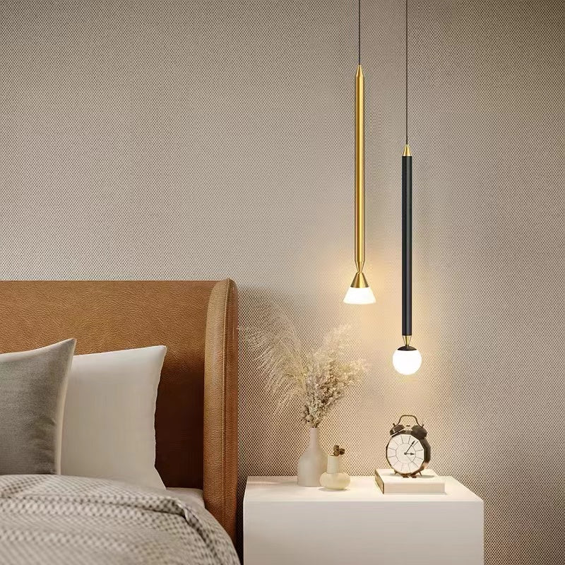 Gold cone-tip and black globe-tip Carr pendants beside a bed above a white nightstand with flowers, a cup, clock and books