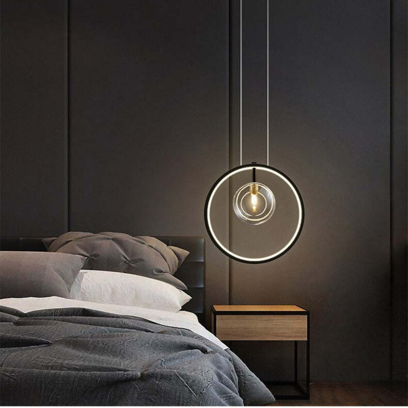 Single-globe black ring pendant beside a grey upholstered bed and wood bedside cabinet