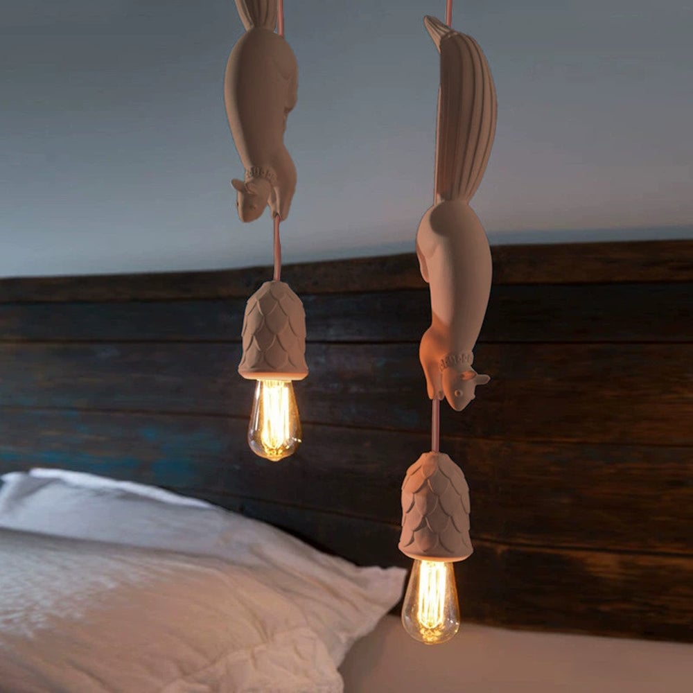 Two pink squirrel pendants beside a bed with a white pillow and dark wooden headboard