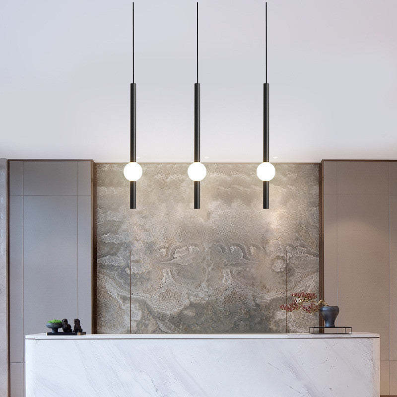Three black-rod Carr pendants with white globes above a counter.
