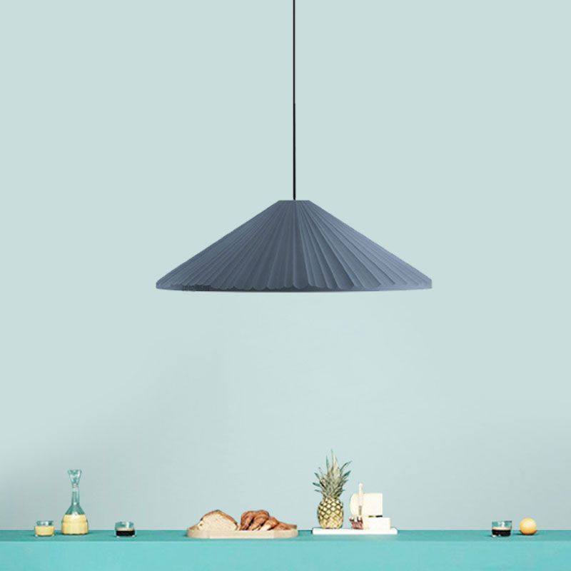 Blue shallow pleated cone pendant against a turquoise wall above a counter with fruit and glassware